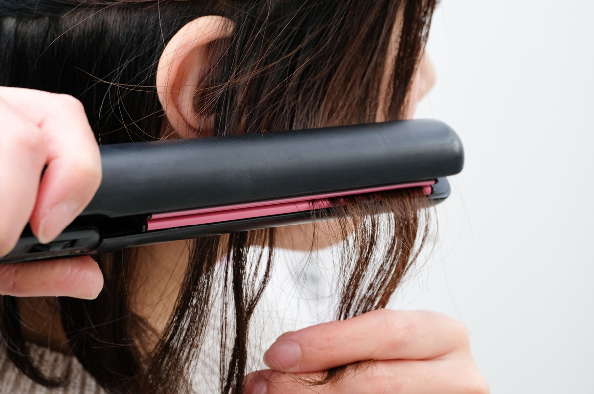 ヘアアイロンで髪を挟んでいる女性のイメージ画像