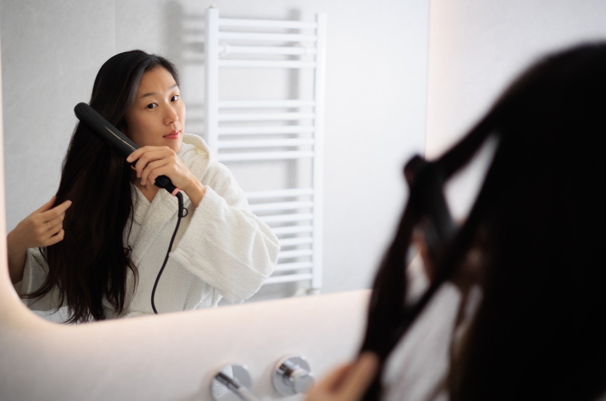 鏡の前でヘアアイロンを使用する女性の画像